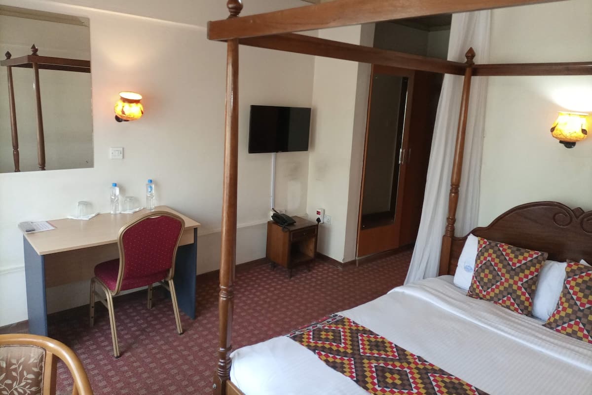 Hotellihuone, jossa on nelipylväinen sänky, työpöytä tuolilla, televisio ja peili.