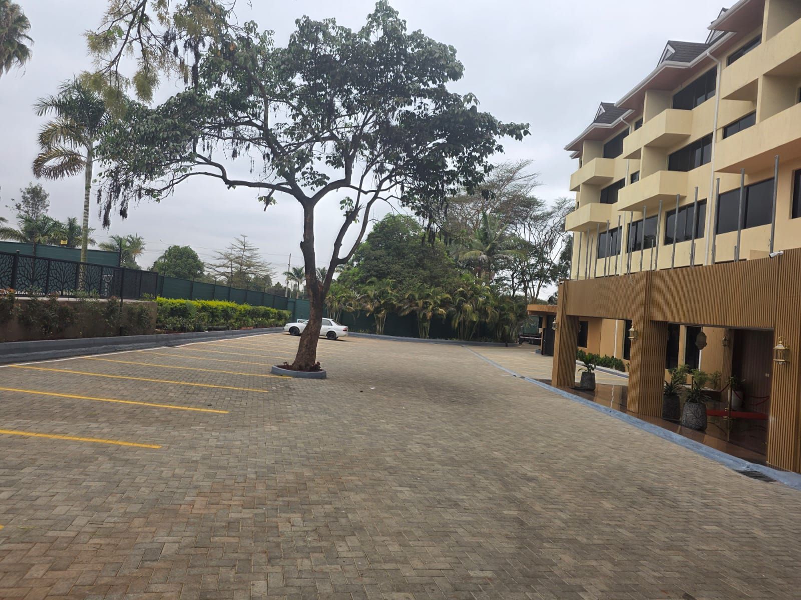 Un estacionamiento con un árbol, un edificio con balcones y una cerca.