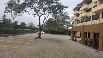 Un estacionamiento con un árbol, un edificio con balcones y una cerca.