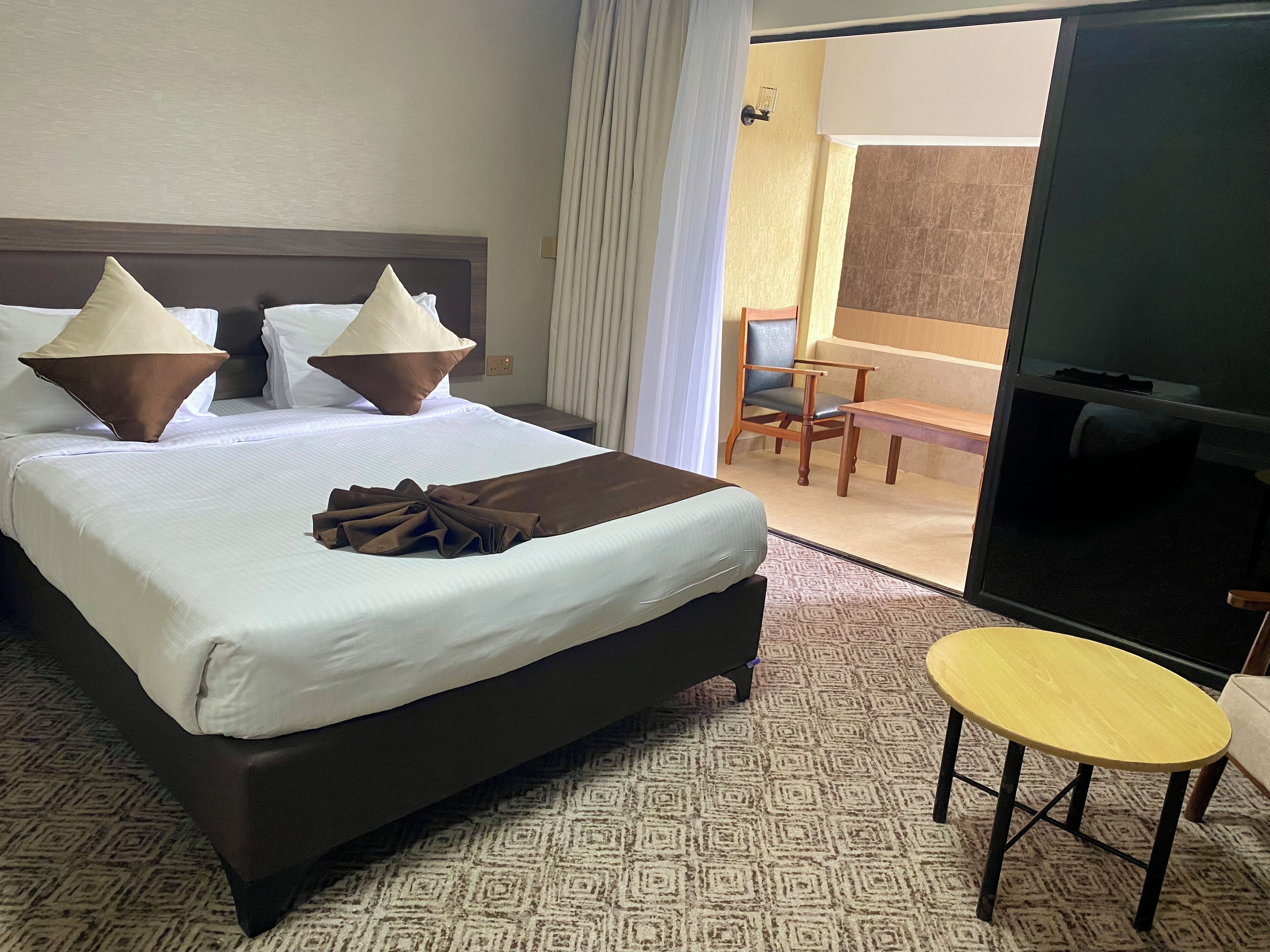 Habitación de hotel con una cama grande, una mesita pequeña, una silla y un televisor.