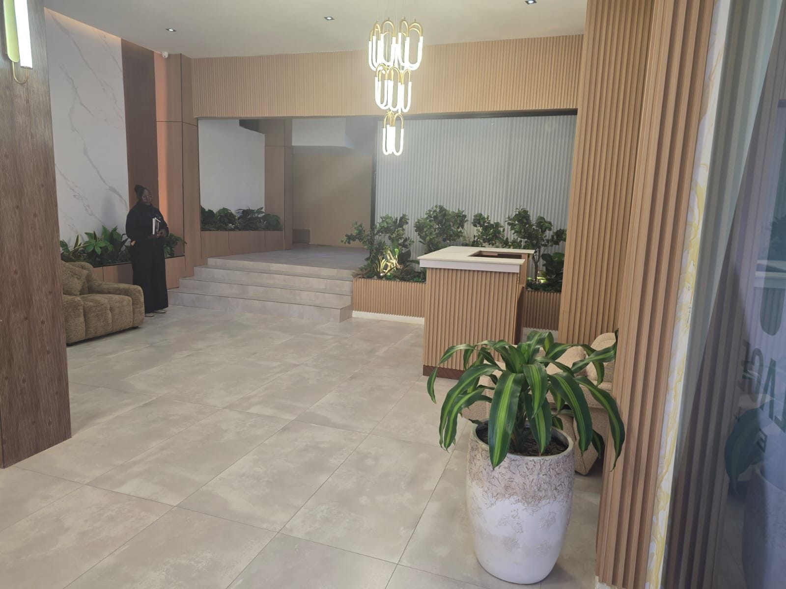 A modern lobby with a reception desk, a staircase, and a potted plant.