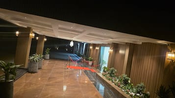 A hotel lobby with a marble floor, potted plants, and a red carpet leading to the entrance.