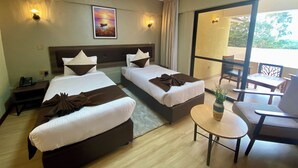 Quarto de hotel com duas camas, uma mesinha, uma cadeira, telefone no criado-mudo e um quadro na parede.