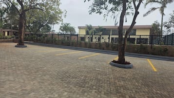 Un estacionamiento pavimentado con espacios delimitados, rodeado de árboles y una valla decorativa.