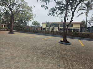 A paved parking area with marked spaces, surrounded by trees and a decorative fence. - Park Place Hotel (Nairobi)
