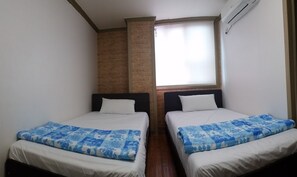 A room with two beds, each with a blue floral bedspread and white pillows. There is a brick wall and a window with a blind.