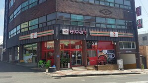 Una tienda de conveniencia 7-Eleven con fachada roja y entrada visible.