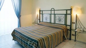 Una cama con colcha a rayas, cabecero metálico con detalles decorativos y una mesita de noche con lámpara.
