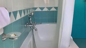 Un baño con una bañera blanca, ducha y pared azul con un diseño geométrico.