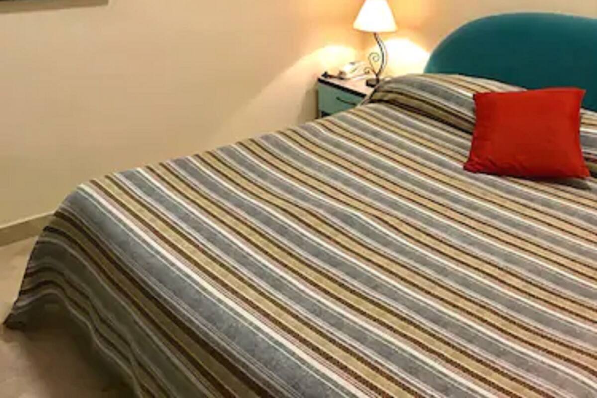A hotel room with a bed, a nightstand, a lamp, a painting on the wall, and a window.
