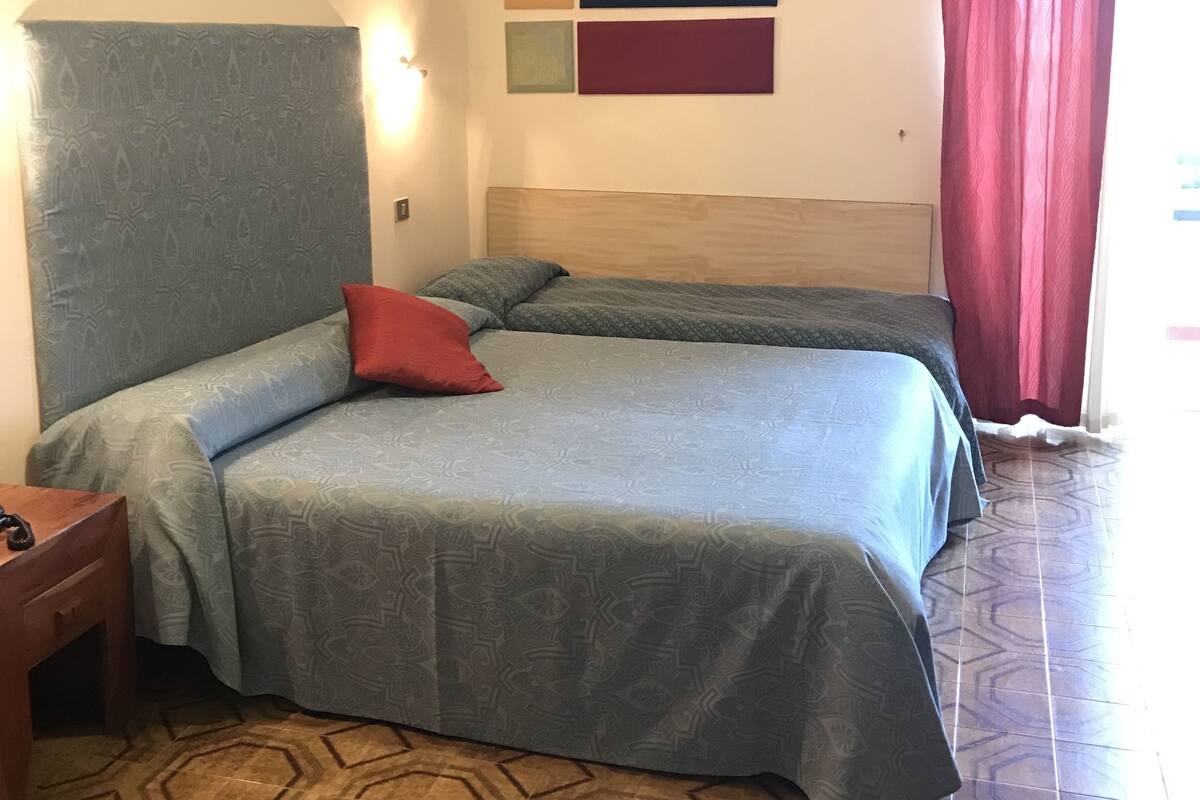 A hotel room with two beds, a wooden headboard, patterned curtains, and a geometric floor design.