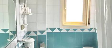 Un baño con un lavamanos grande, un espejo, una ventana con persianas y un taburete pequeño.