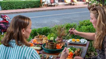Two people dining outdoors with a variety of dishes and a table set with chopsticks and a teapot.