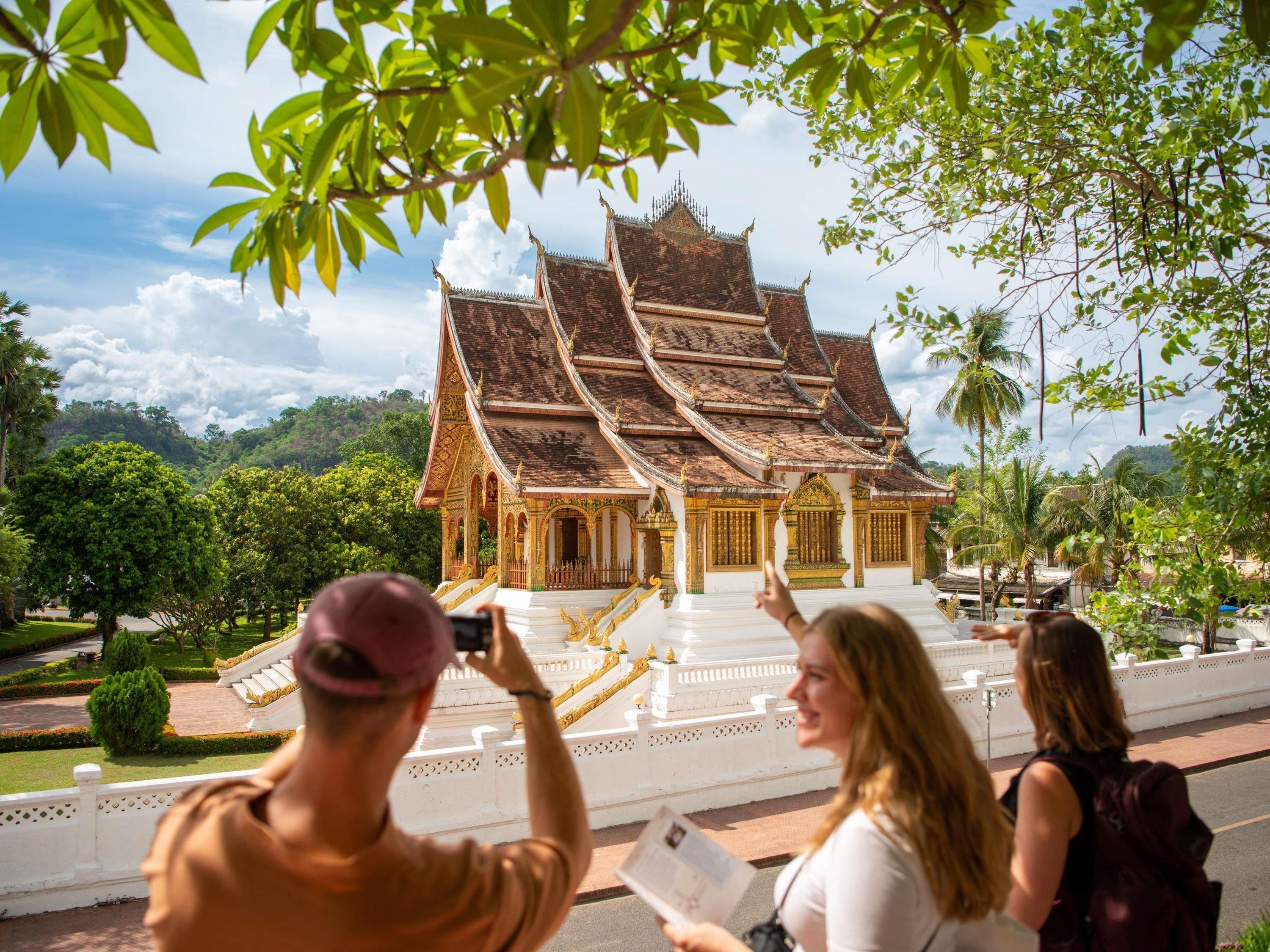A traditional multi-tiered temple with ornate golden decorations, surrounded by lush greenery and a clear sky.