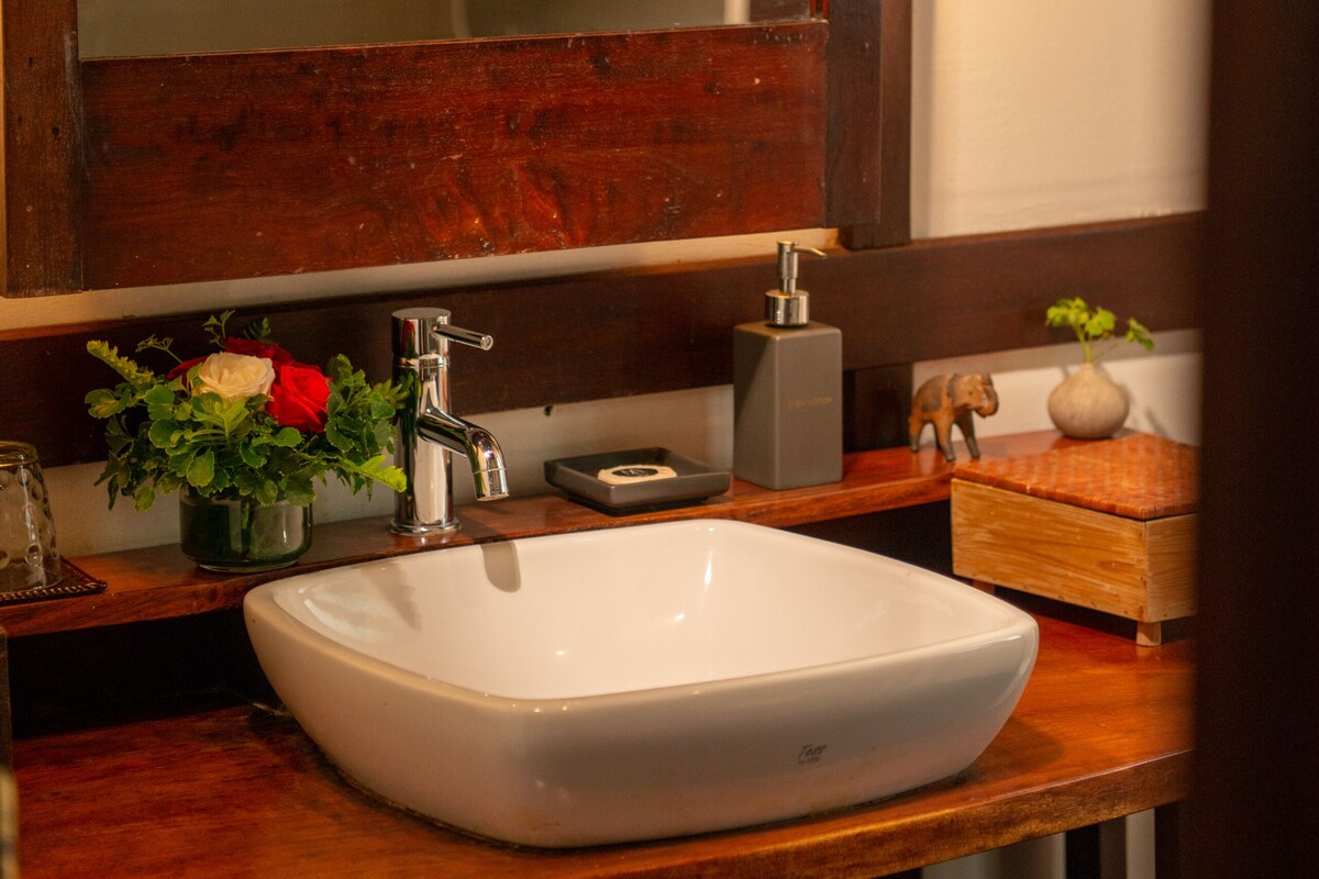A bathroom with a wooden vanity, a white sink, a mirror, and a decorative vase with flowers.