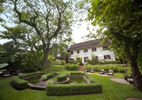 A well-maintained garden with a pond, seating areas, and a white building with a brown roof.