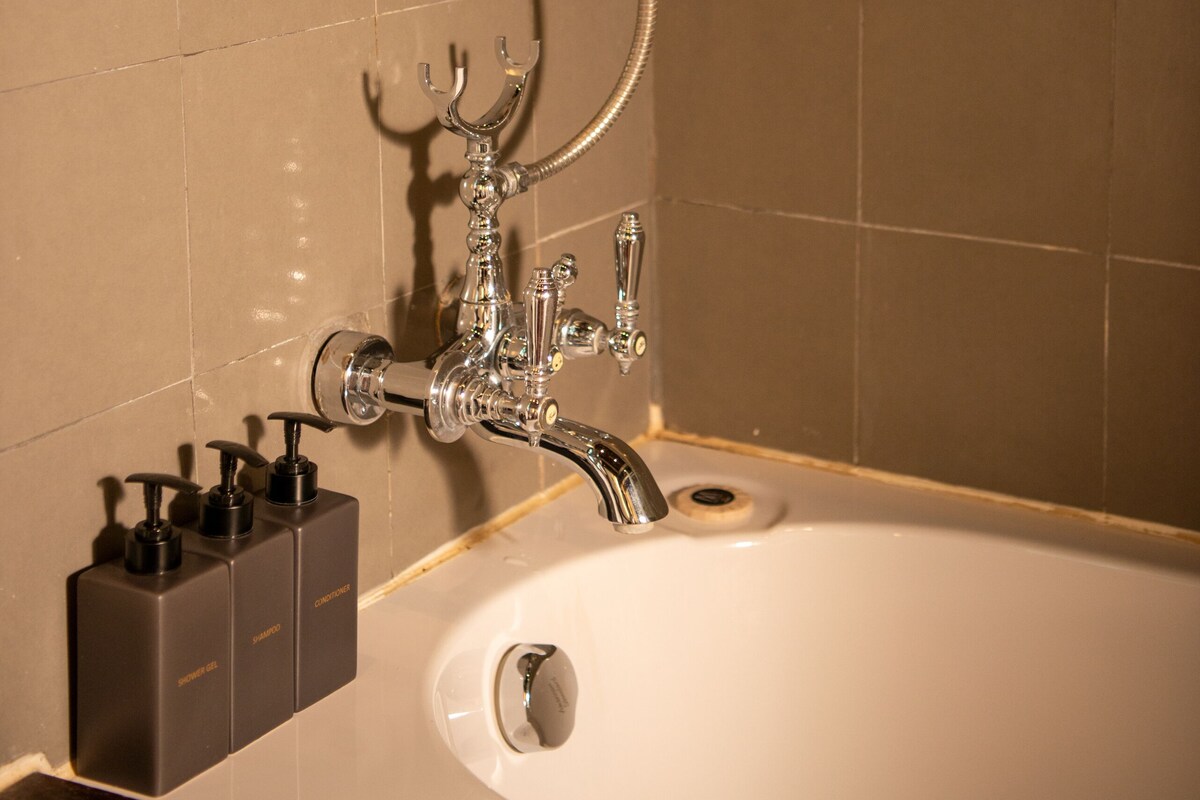 A bathroom with a bathtub, a shower head, and a set of soap dispensers.