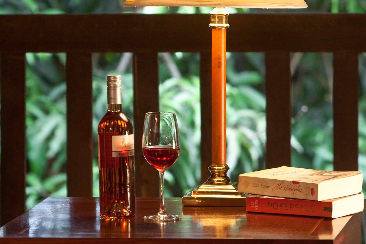 A wooden table with a wine bottle, a glass of red wine, a lamp, and books.