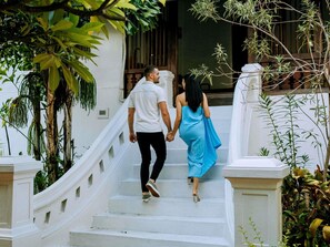 Um casal caminhando por uma escadaria branca com corrimão, cercado por vegetação.