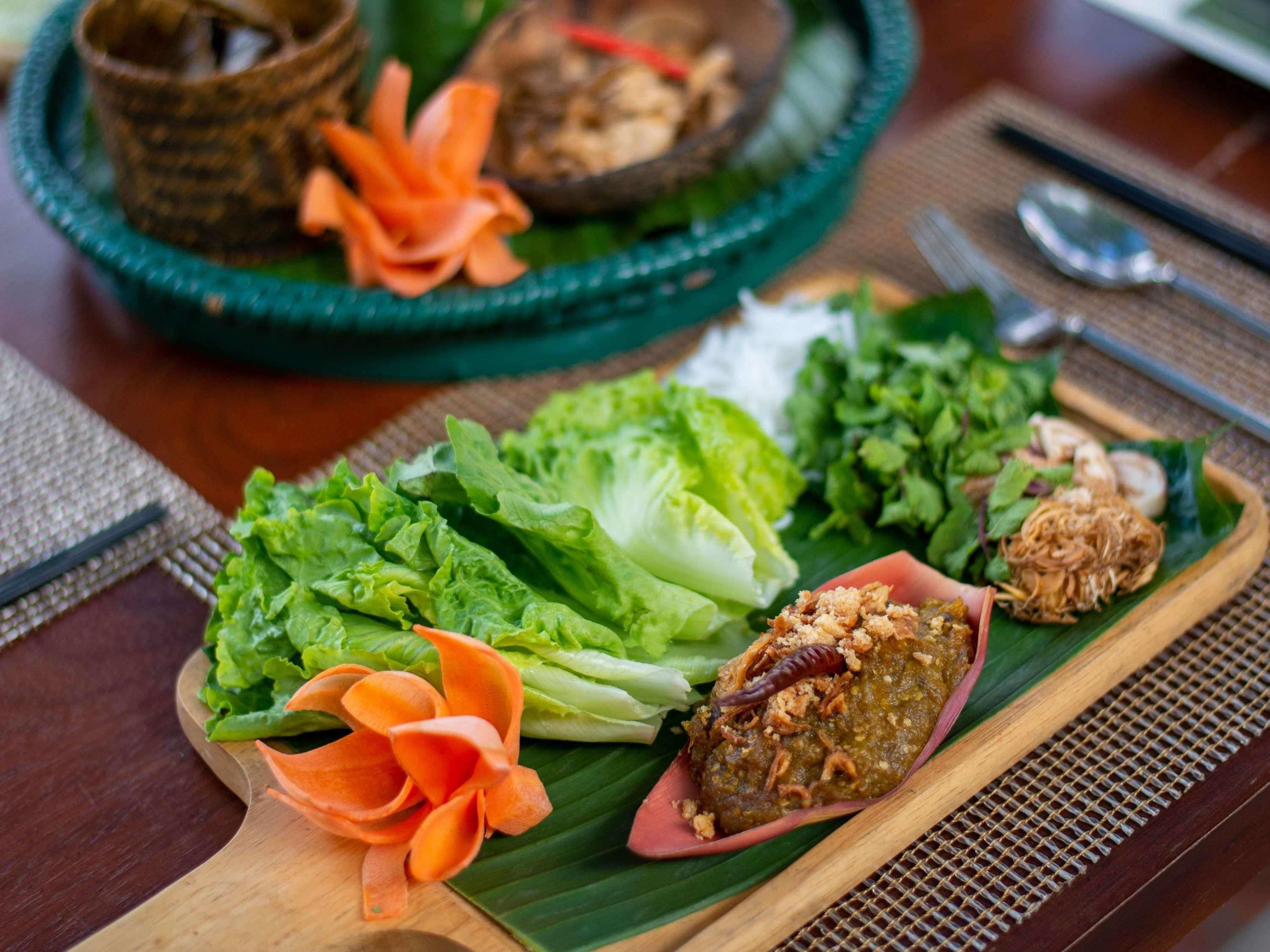 A wooden serving board with various dishes including lettuce, a carrot flower, and a bowl of soup.