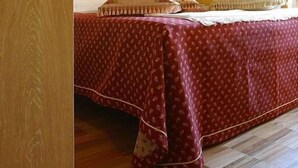 A bedroom with a wooden ceiling, a bed with a red patterned bedspread, a nightstand with a lamp, and a wall-mounted light fixture. - Albergo Morandi (Reggio nell'Emilia)