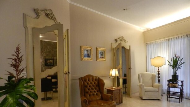 A spacious living room with a large armchair, a smaller armchair, a side table with a lamp, and a mirror on the wall. - Albergo Morandi (Reggio nell'Emilia)