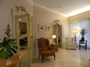A spacious living room with a large armchair, a smaller armchair, a side table with a lamp, and a mirror on the wall. - Albergo Morandi (Reggio nell'Emilia)