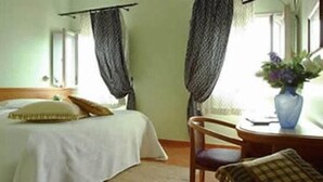 A bedroom with a bed, a chair, a table, and a vase with flowers. - Albergo Morandi (Reggio nell'Emilia)