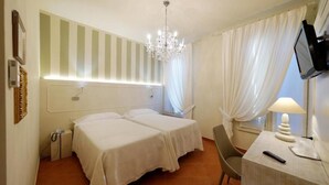 A hotel room with two beds, a desk with a lamp, a TV, and a chandelier. - Albergo Morandi (Reggio nell'Emilia)