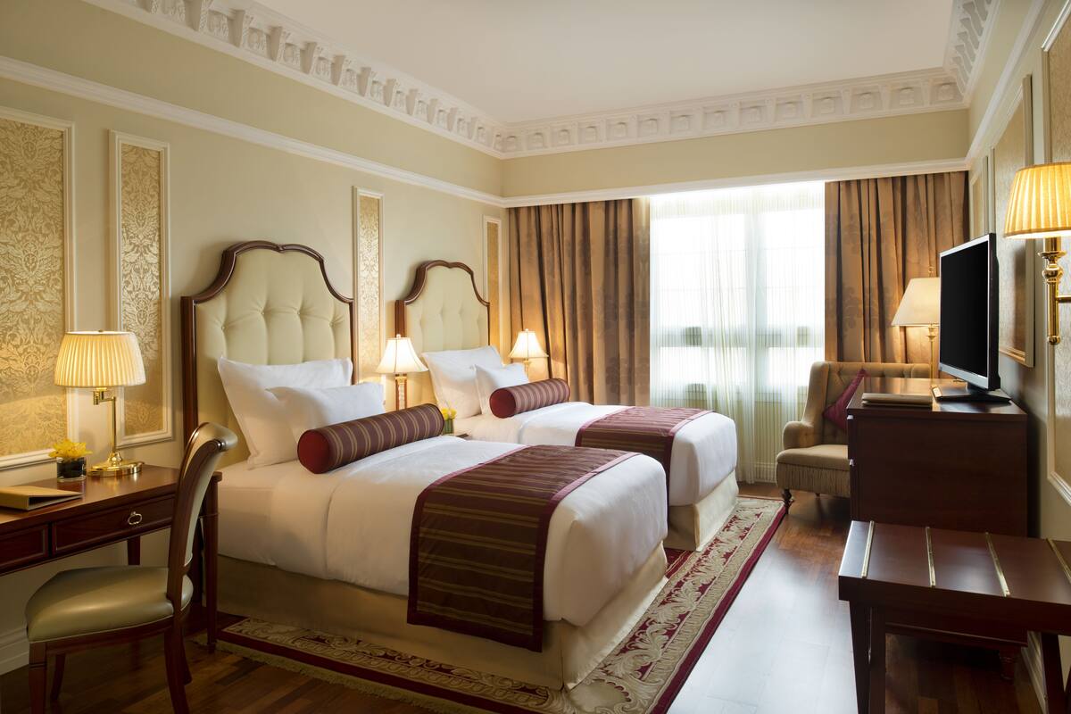A hotel room with two beds, a desk, a chair, a television, and a window with curtains.