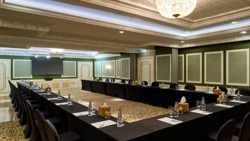 A conference room with a long table, chairs, a chandelier, and a television screen.