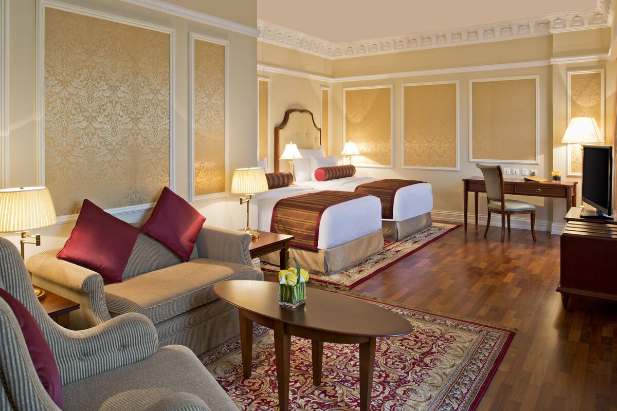 A hotel room with a bed, two bedside tables, a desk, a chair, a sofa, and a coffee table.