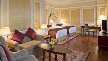 A hotel room with a bed, two bedside tables, a desk, a chair, a sofa, and a coffee table.