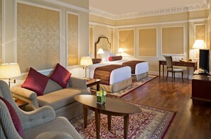 A hotel room with a bed, two bedside tables, a desk, a chair, a sofa, and a coffee table.