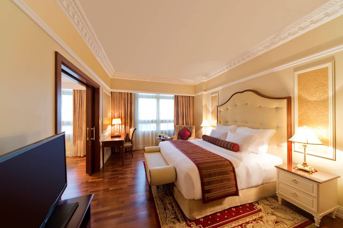 A hotel room with a large bed, a TV, a desk with a chair, and a window with curtains.