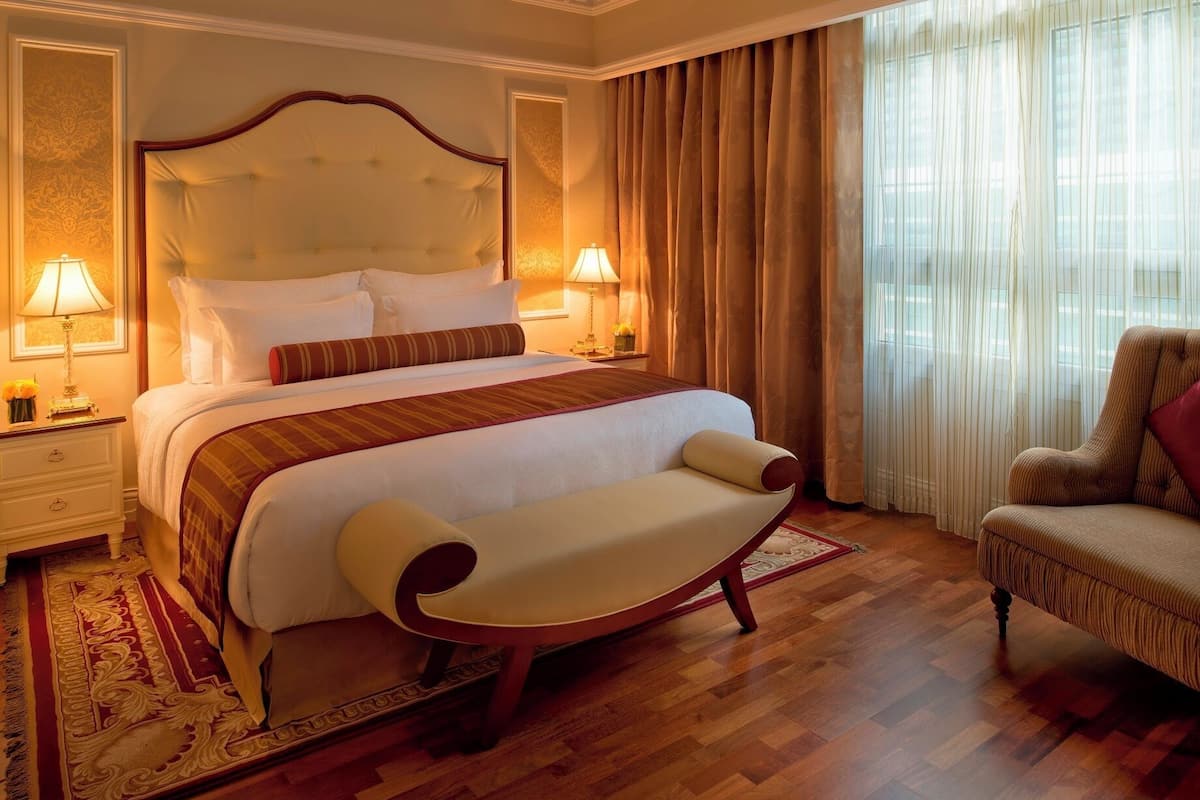 A hotel room with a large bed, two bedside lamps, a chair, and a window with curtains.