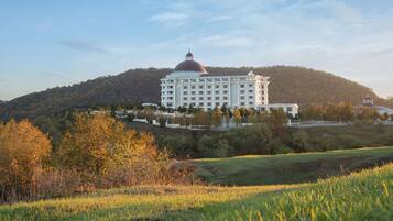 A large, white building with a dome and multiple floors, surrounded by trees and hills.