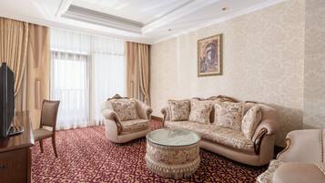 Un salon spacieux comprenant un canapé, des fauteuils, une table basse en verre et un téléviseur.