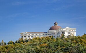A large, white building with a prominent dome and a smaller dome on top, surrounded by dense green foliage.