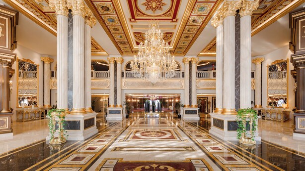 Un lobby imponente con suelos de mármol, columnas ornamentales y una gran araña.