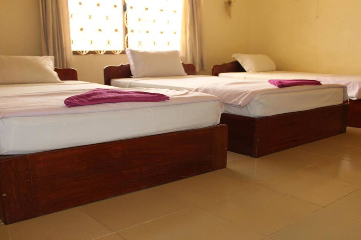Una habitación de hotel con tres camas de madera, cada una con ropa blanca y una toalla morada.