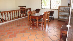 Un coin repas avec une table et des chaises en bois, un escalier avec une rampe en bois et une fenêtre agrémentée de rideaux à motifs.