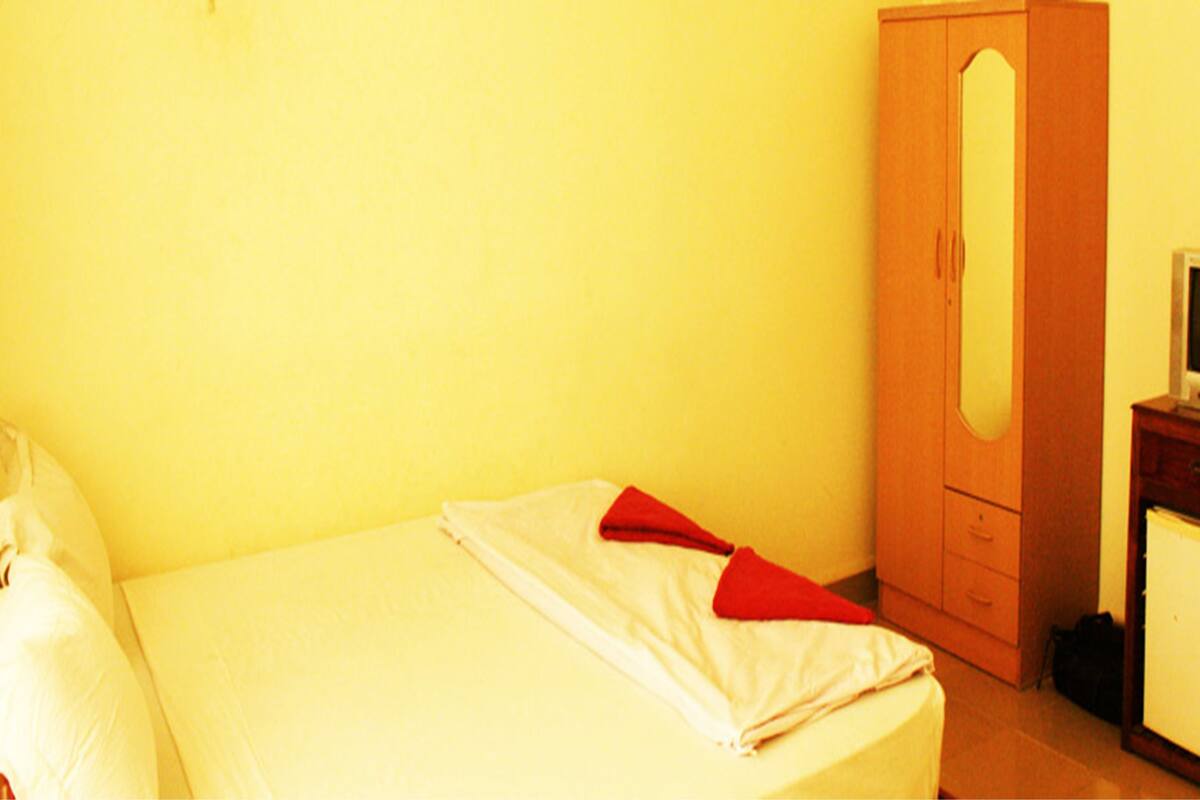 Una habitación pequeña con una cama individual, un armario de madera y un televisor pequeño sobre un mueble.