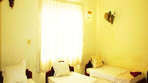 Une chambre avec deux lits simples, une fenêtre avec des rideaux légers, un luminaire fixé au mur et un petit élément de décoration murale.