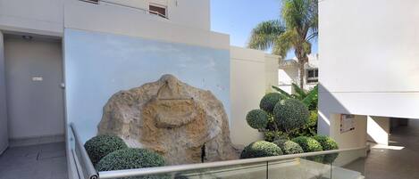 A modern building with a glass railing, a large rock sculpture, and neatly trimmed bushes.
