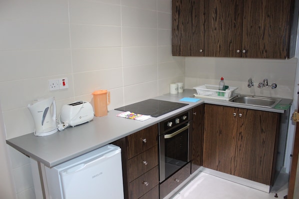 A compact kitchen with a built-in oven, a toaster, and a refrigerator. - Petsas Apartments & Tavern (Pegeia)