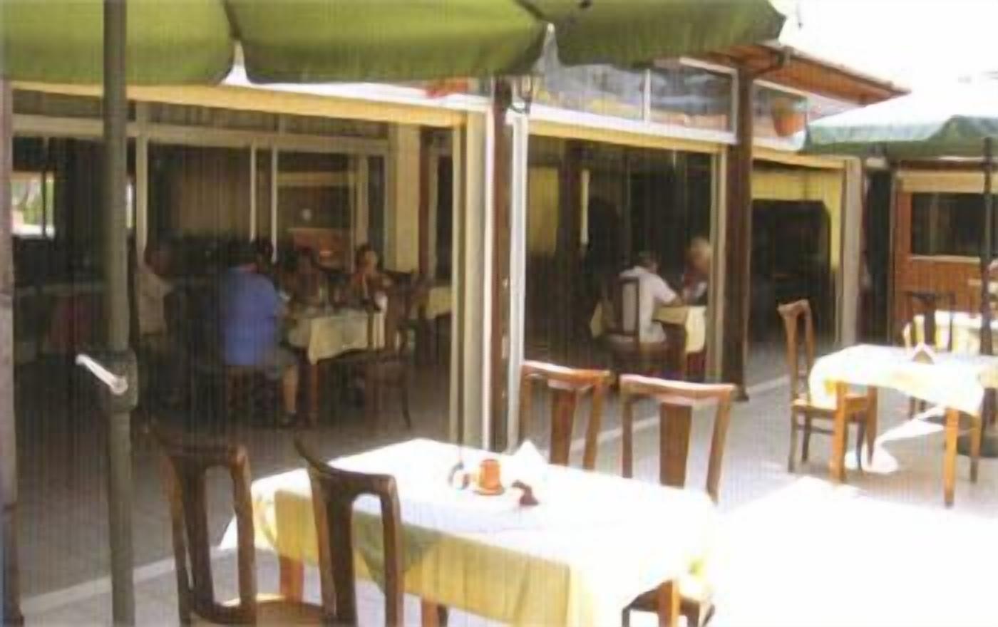 An outdoor dining area with tables and chairs, covered by a green umbrella.