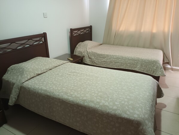 Two single beds with wooden headboards, a small bedside table, and a curtain. - Petsas Apartments & Tavern (Pegeia)