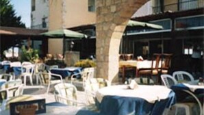 Een terras met tafels en stoelen, een stenen boog en een gebouw op de achtergrond.