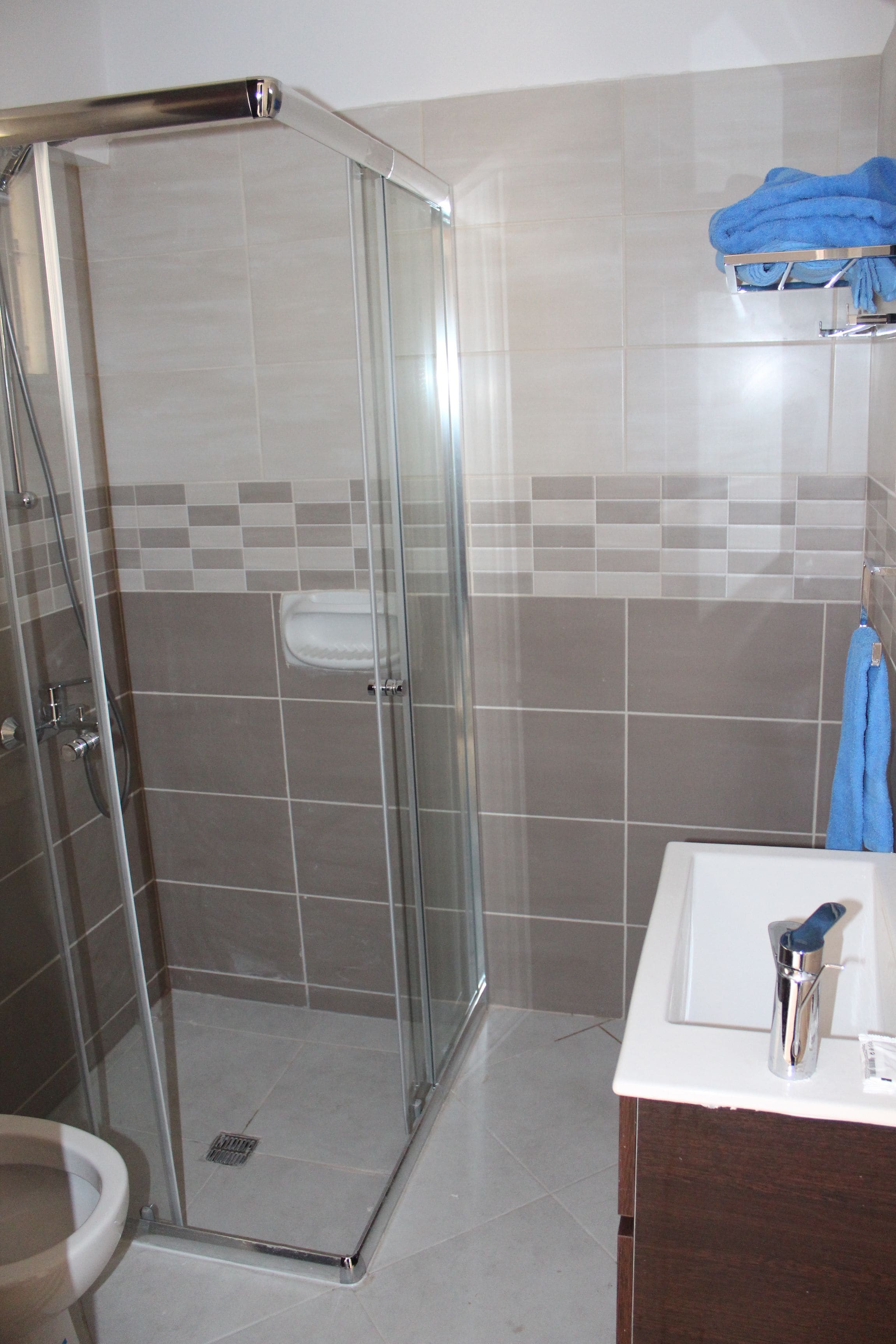 Un baño con ducha envuelta en vidrio, un lavabo blanco y una toalla azul en un perchero.